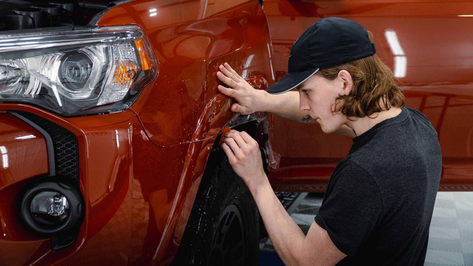 Mechanic inspecting the front fender of a red SUV in a garage
