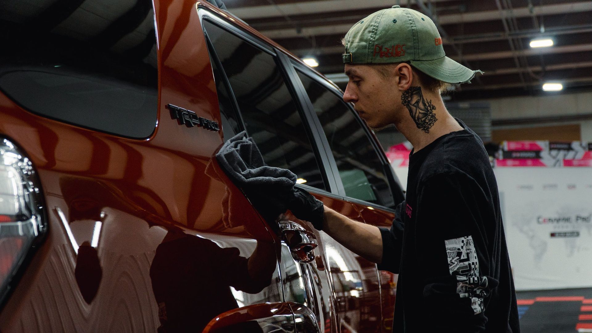 Person in a green cap inspecting a red car with its trunk open at an auto show