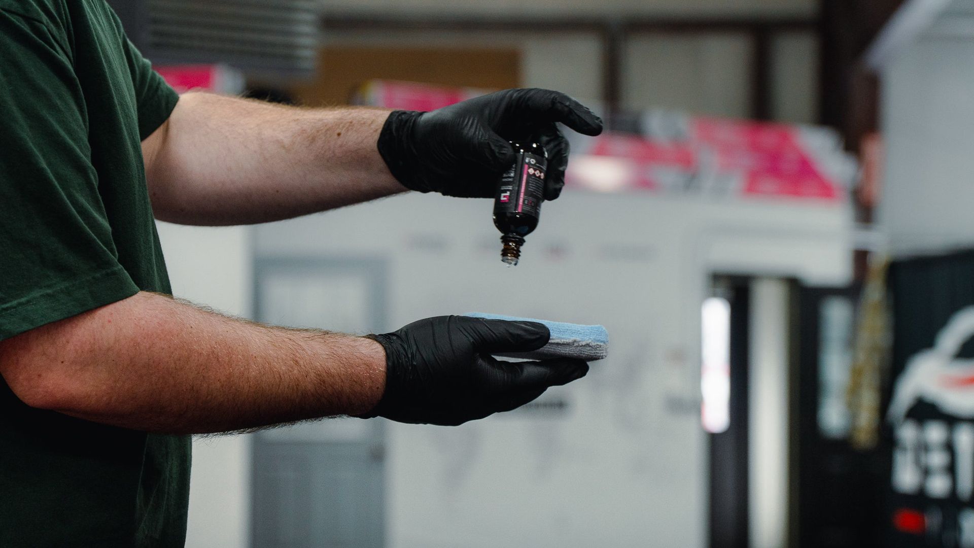 Gloved hands holding and dripping a dark liquid in an indoor lab or workshop setting
