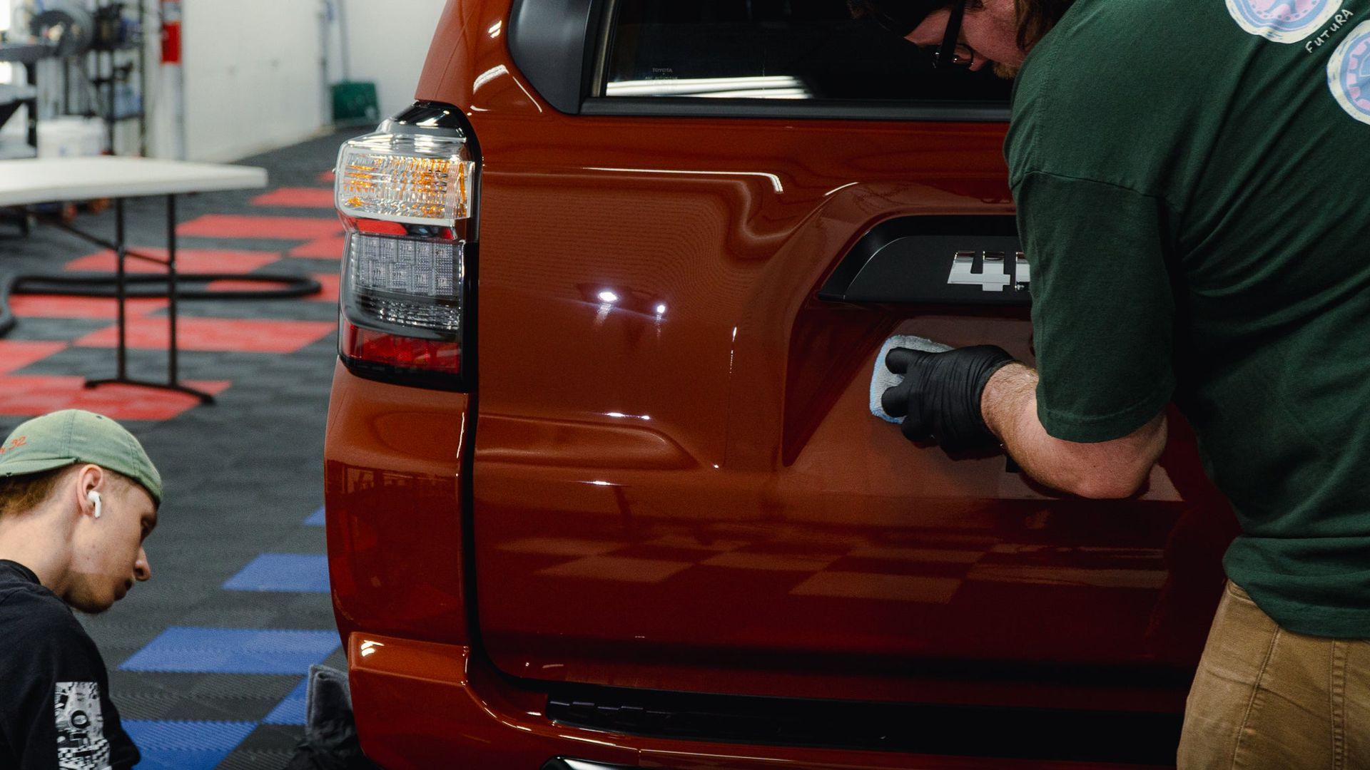 Two people installing a rear badge on a red SUV in a workshop