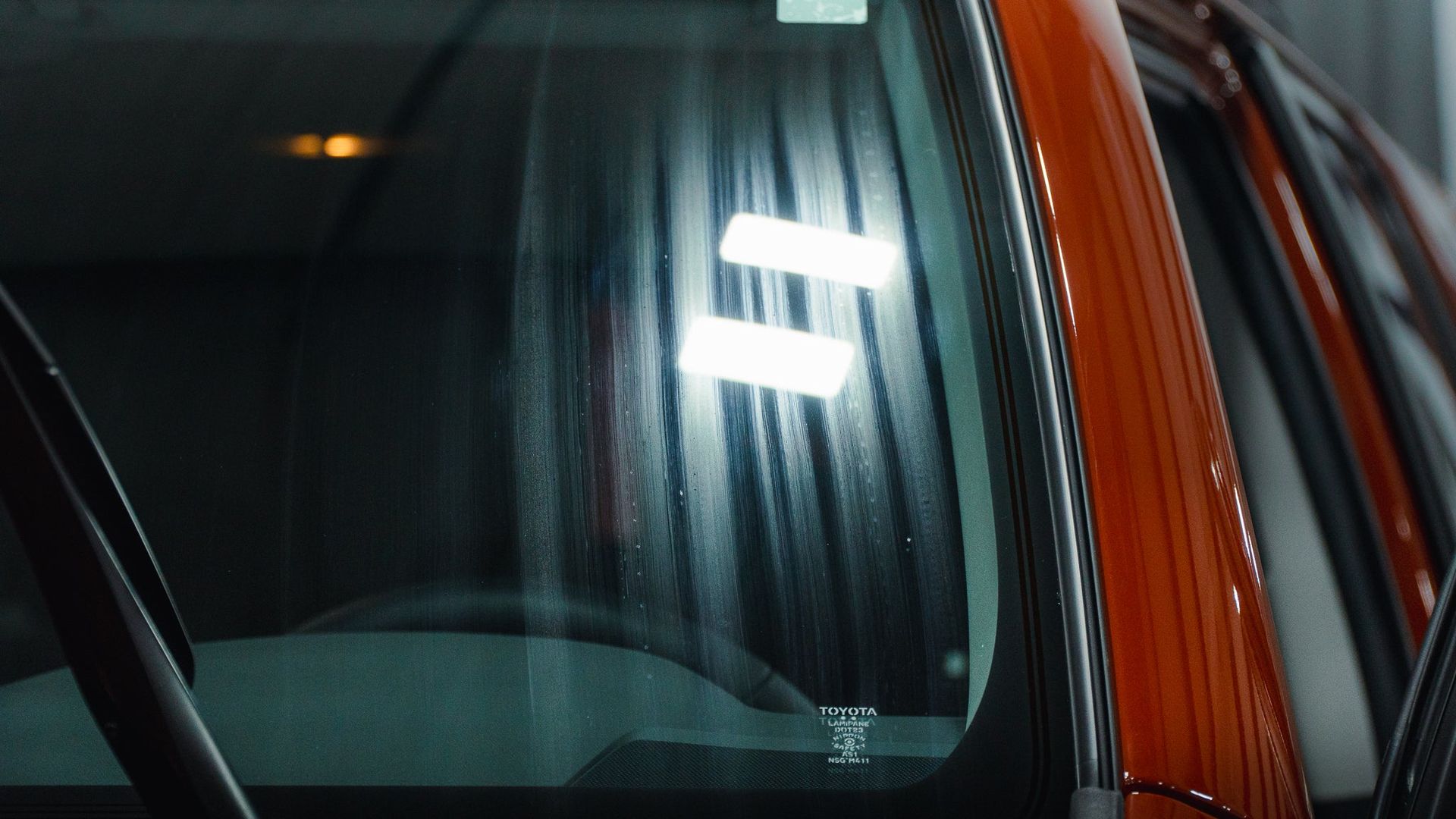 Close-up of a red car windshield reflecting bright lights at night