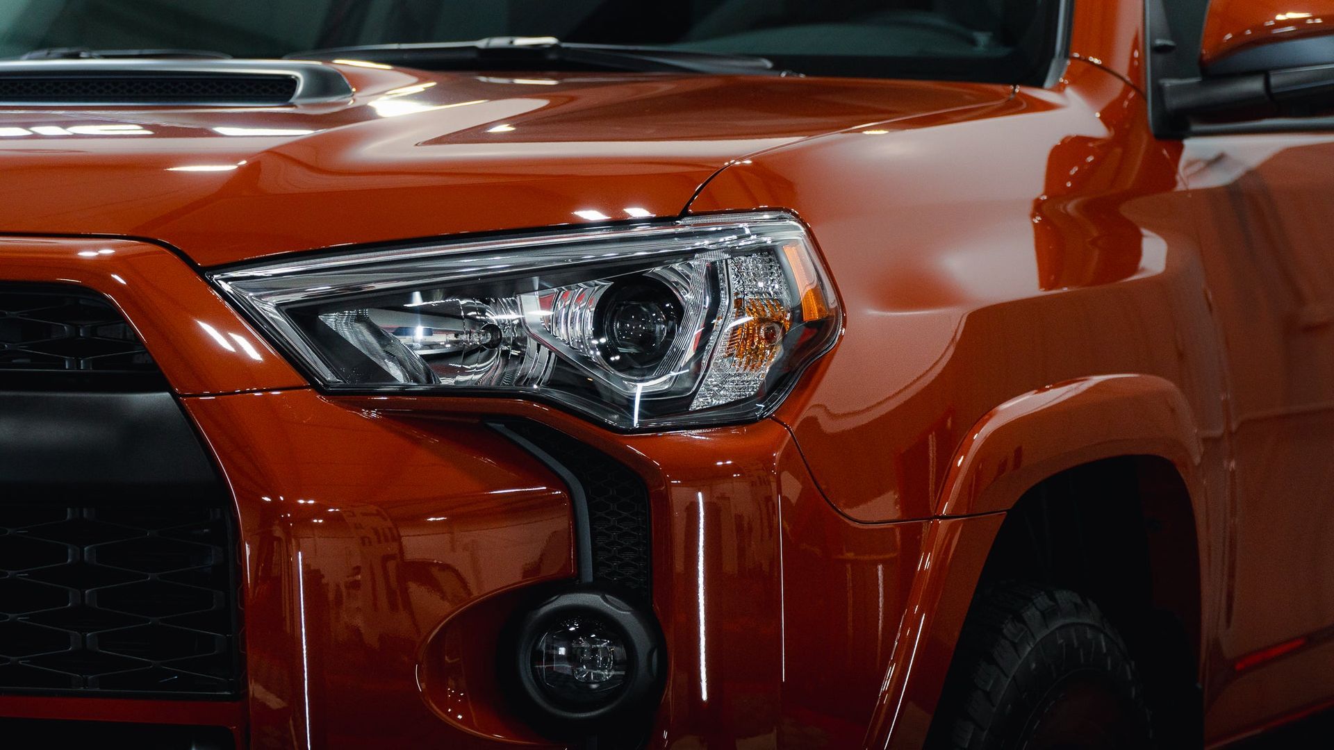 Close-up of an orange pickup truck’s front headlight and grille