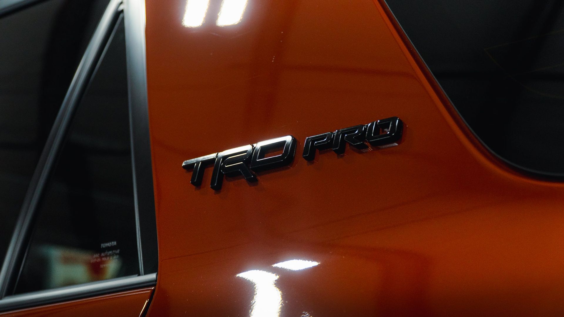 Close-up of an orange car’s side with a black “TRD Pro” badge and window trim