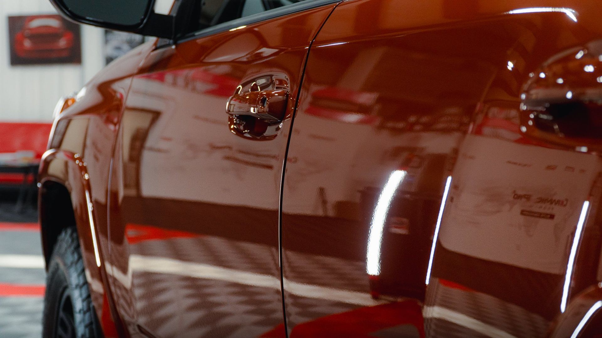Close-up of a glossy red car door with reflections in an indoor showroom