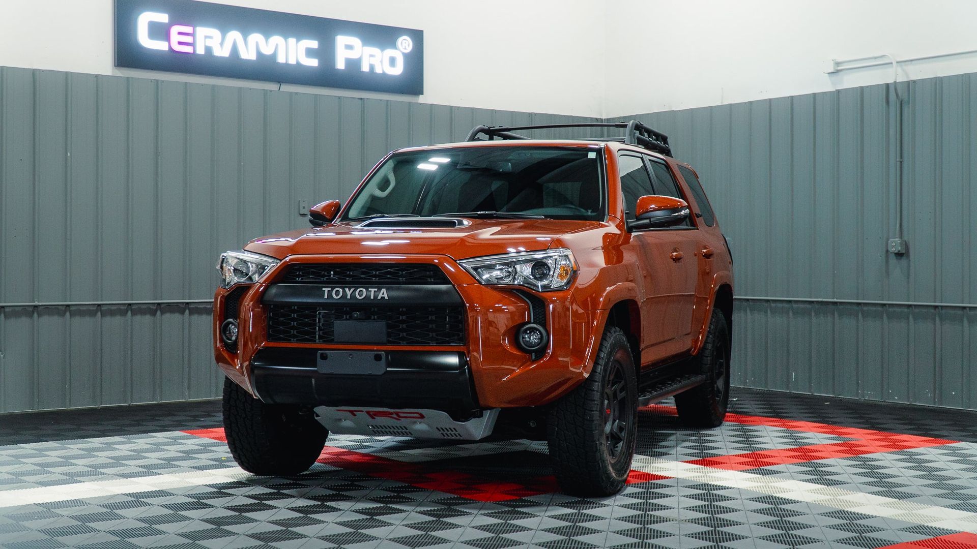 Orange Toyota pickup on display in a Ceramic Pro showroom, with black trim and off-road tires.