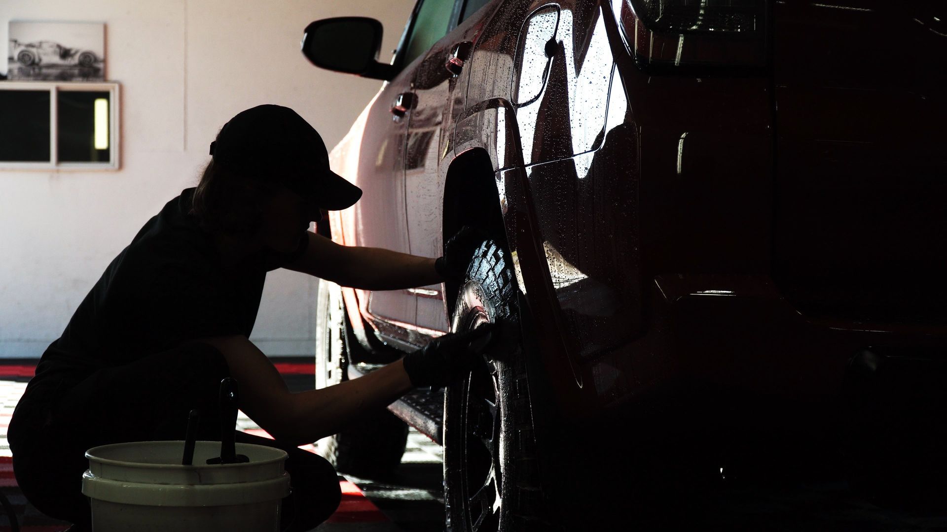 Silhouetted mechanic polishing a car wheel in a dim garage