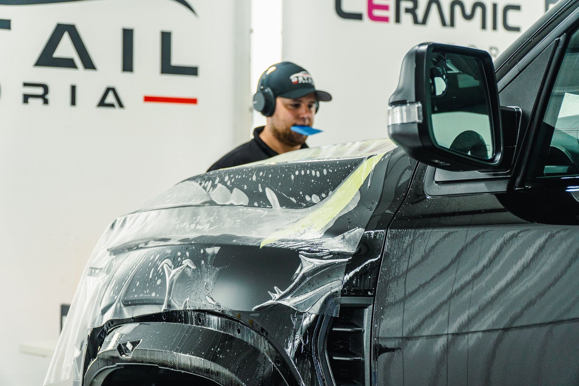Detailer polishing a black car in a ceramic coating shop