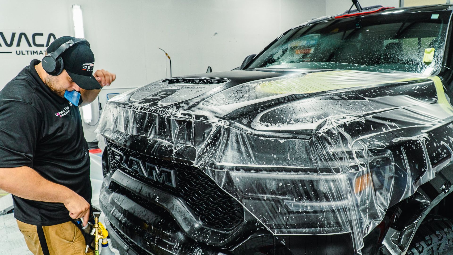 Detailer power-washing a black truck covered in soap suds in a car wash bay