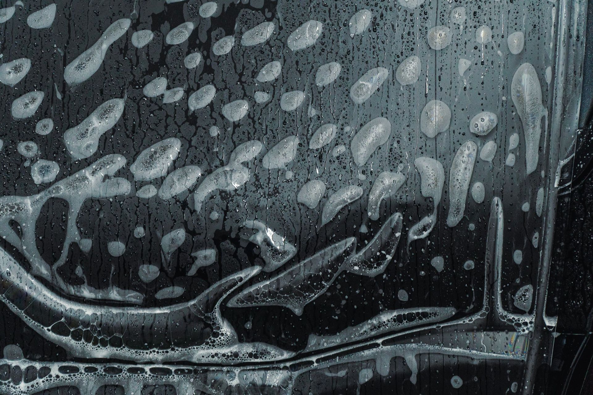 Rain-covered car windshield with water droplets and blurred reflections