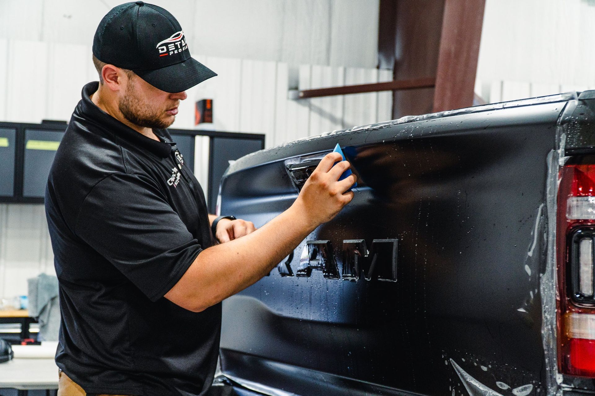 Man applying a decal to the side of a black truck in a workshop