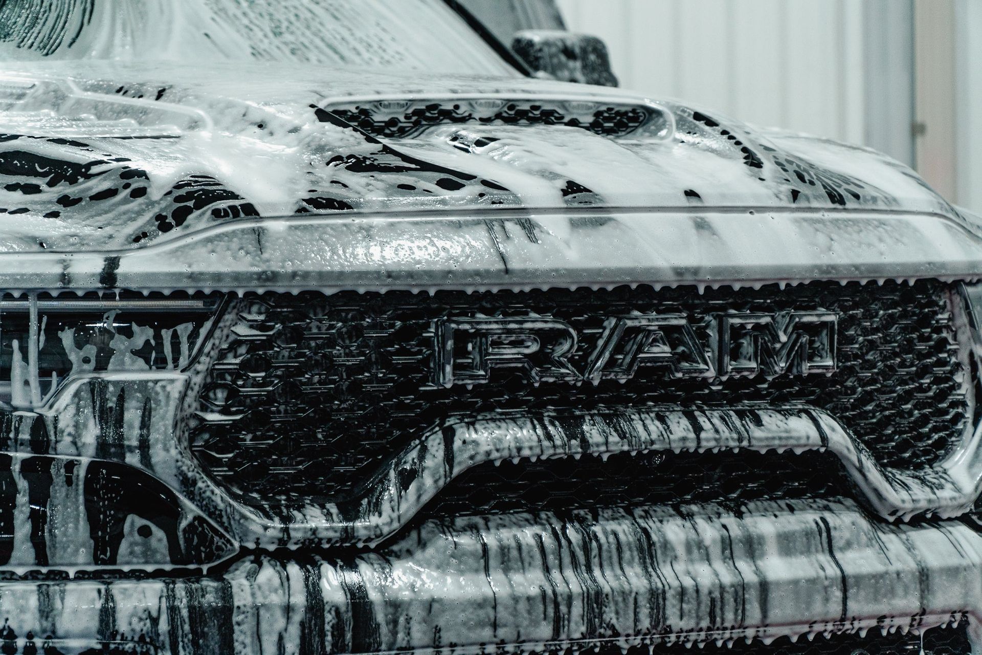 Front view of a black car covered in thick white soap suds during a wash