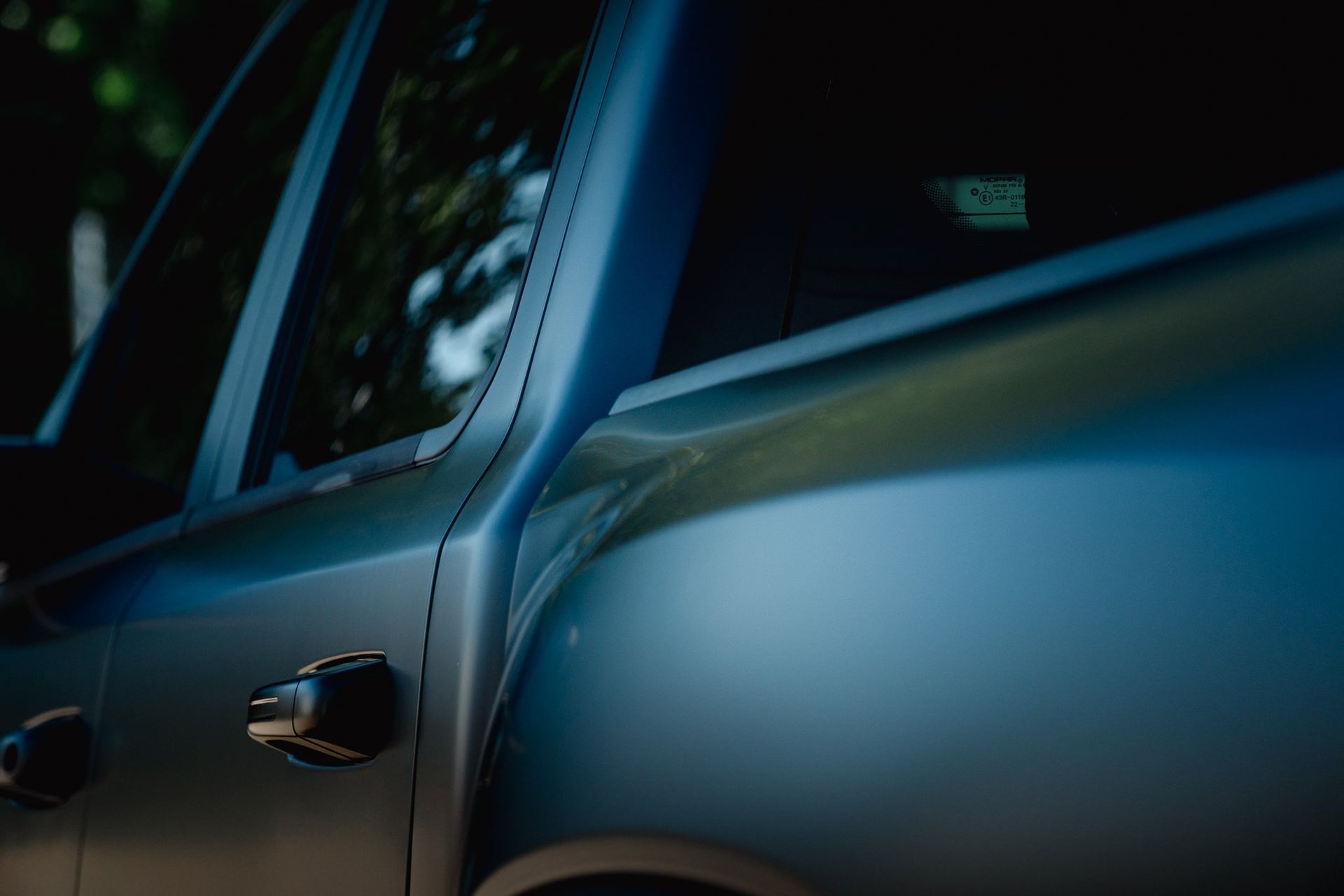 Close-up of a dark blue car door and side mirror with reflections of trees in the window.