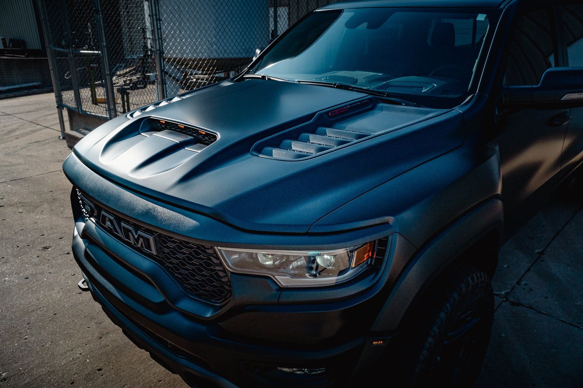 Dark blue pickup truck parked outdoors by a chain-link fence, front view.