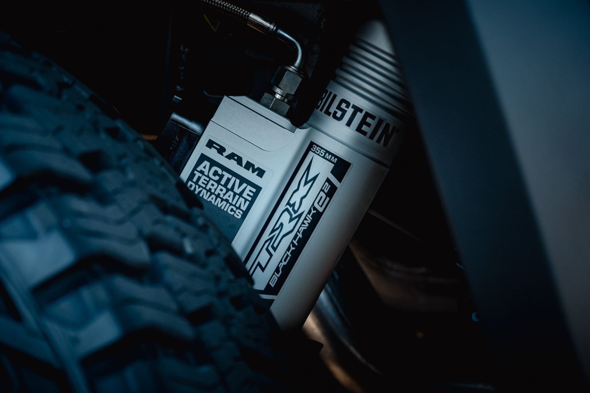 Close-up of a dirt bike rear suspension and tire in dim blue light.