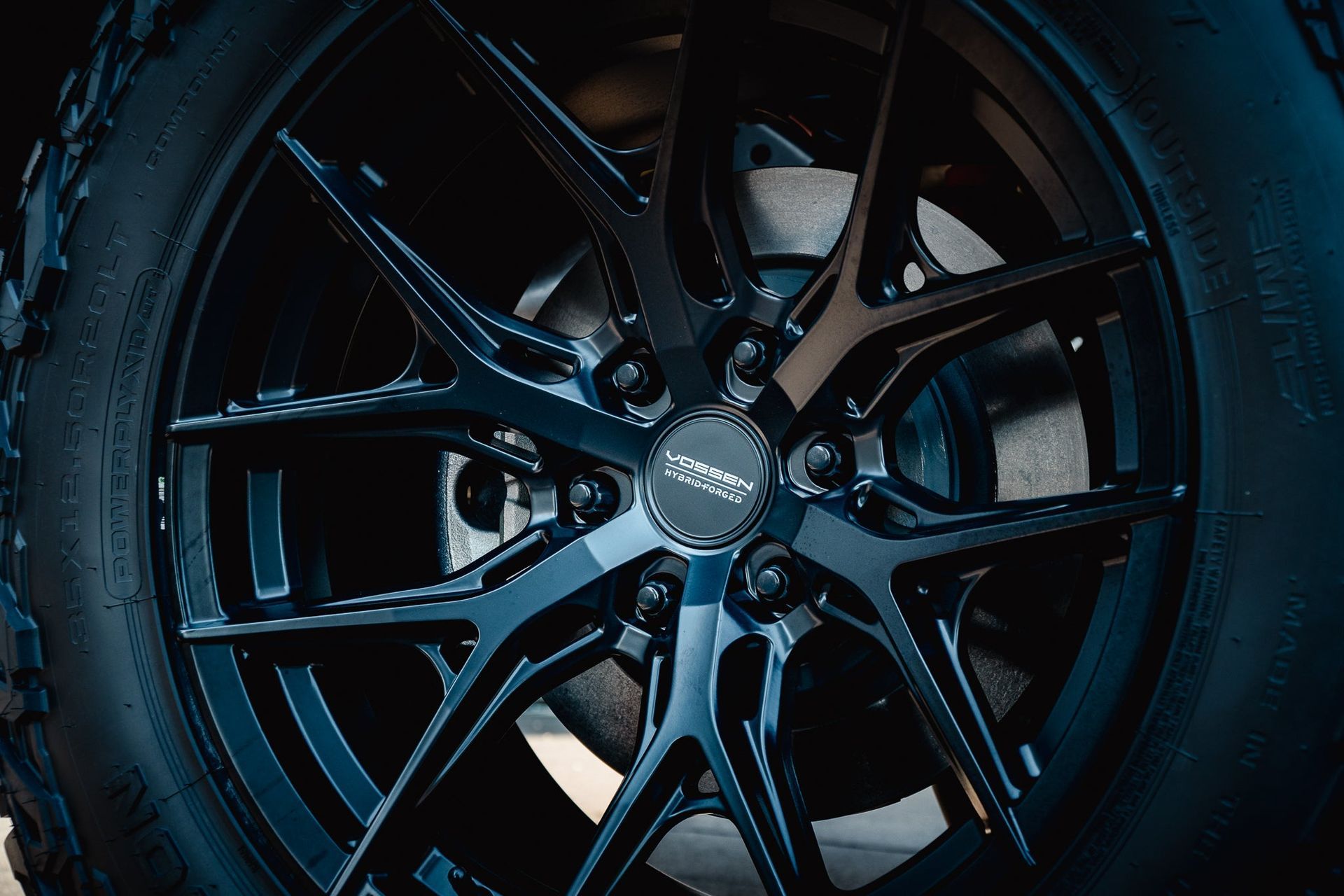 Close-up of a glossy black alloy wheel with blue highlights in dim lighting