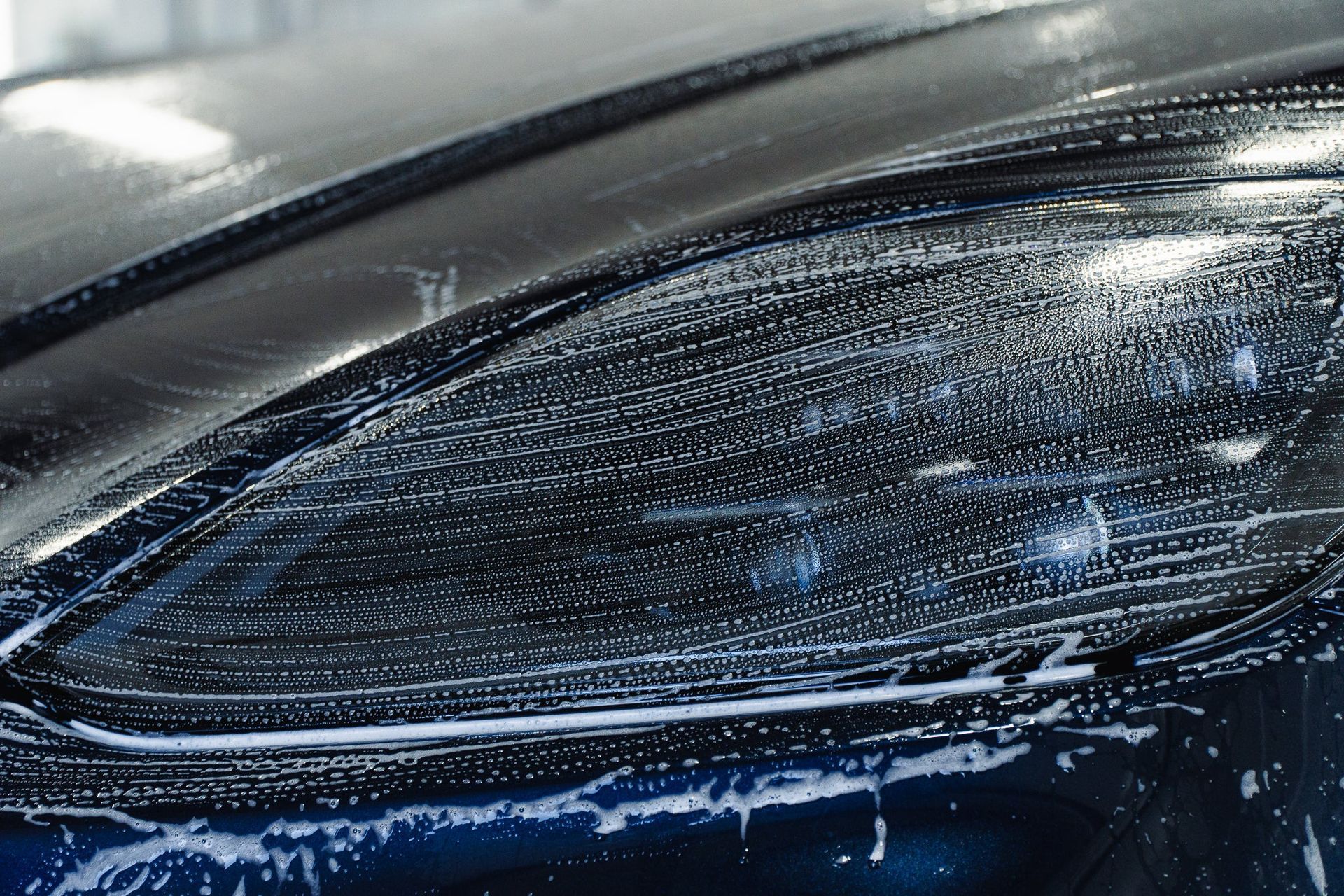 Close-up of a dark car’s headlight covered in water droplets and soap suds