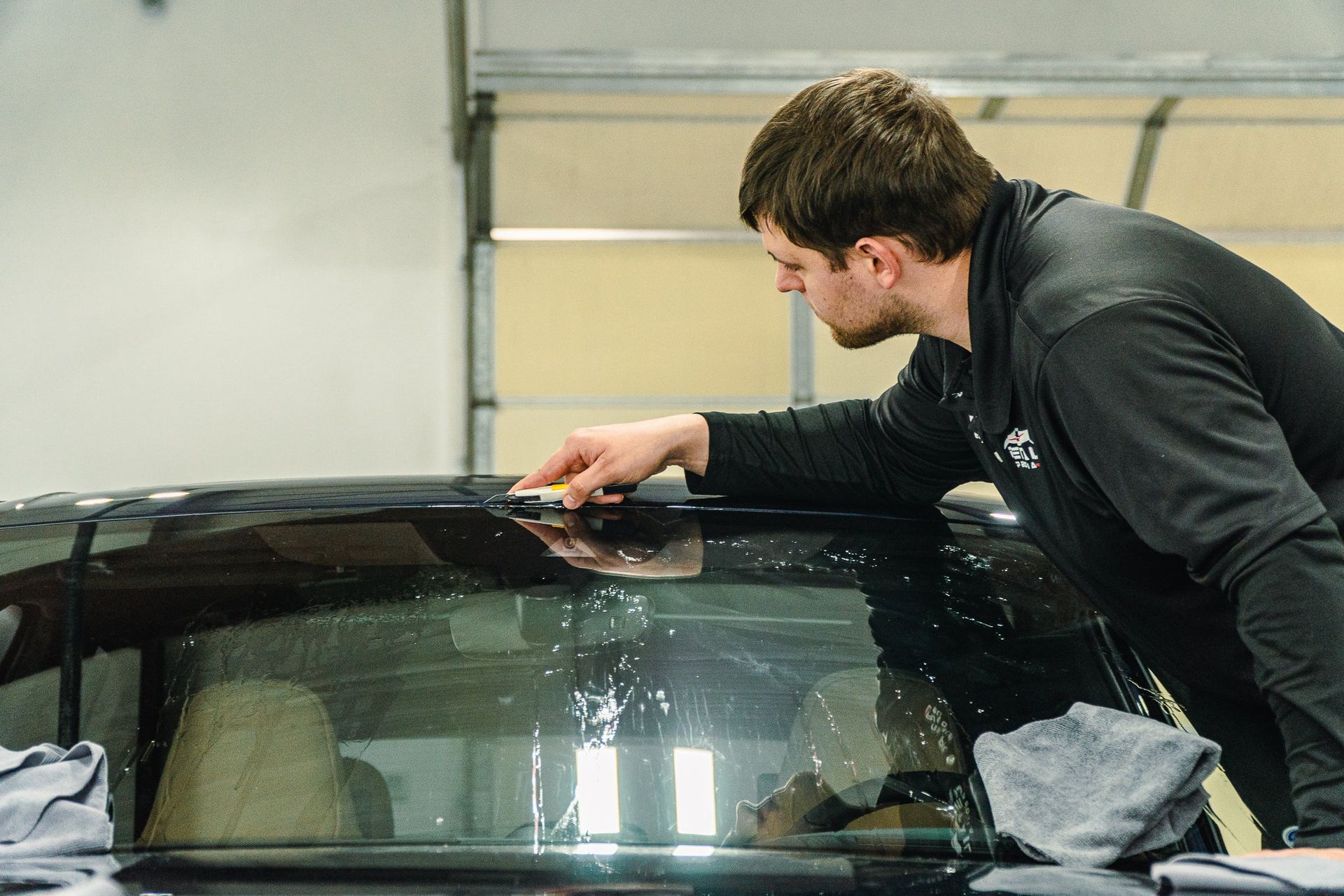 Man polishing a car windshield in a garage using a cloth and tool