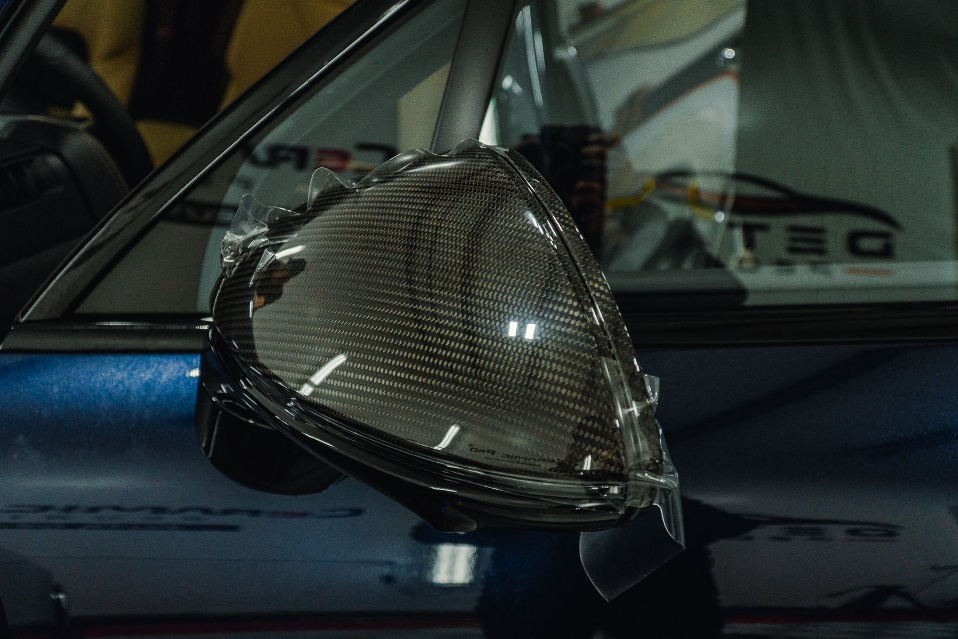 Carbon fiber side mirror on a dark blue car, damaged and taped, shown close-up.