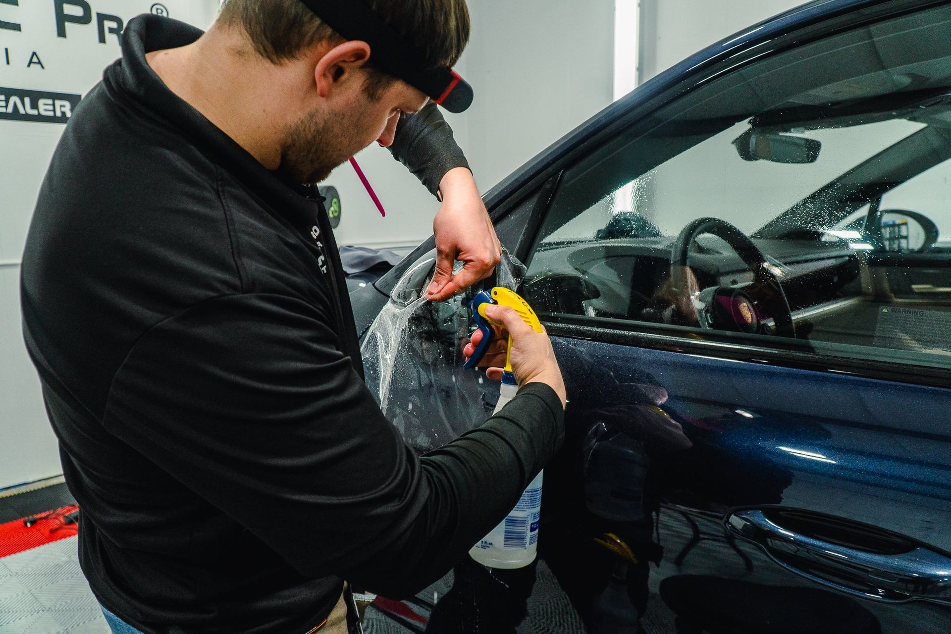 Person wrapping protective film on a blue car door in a garage