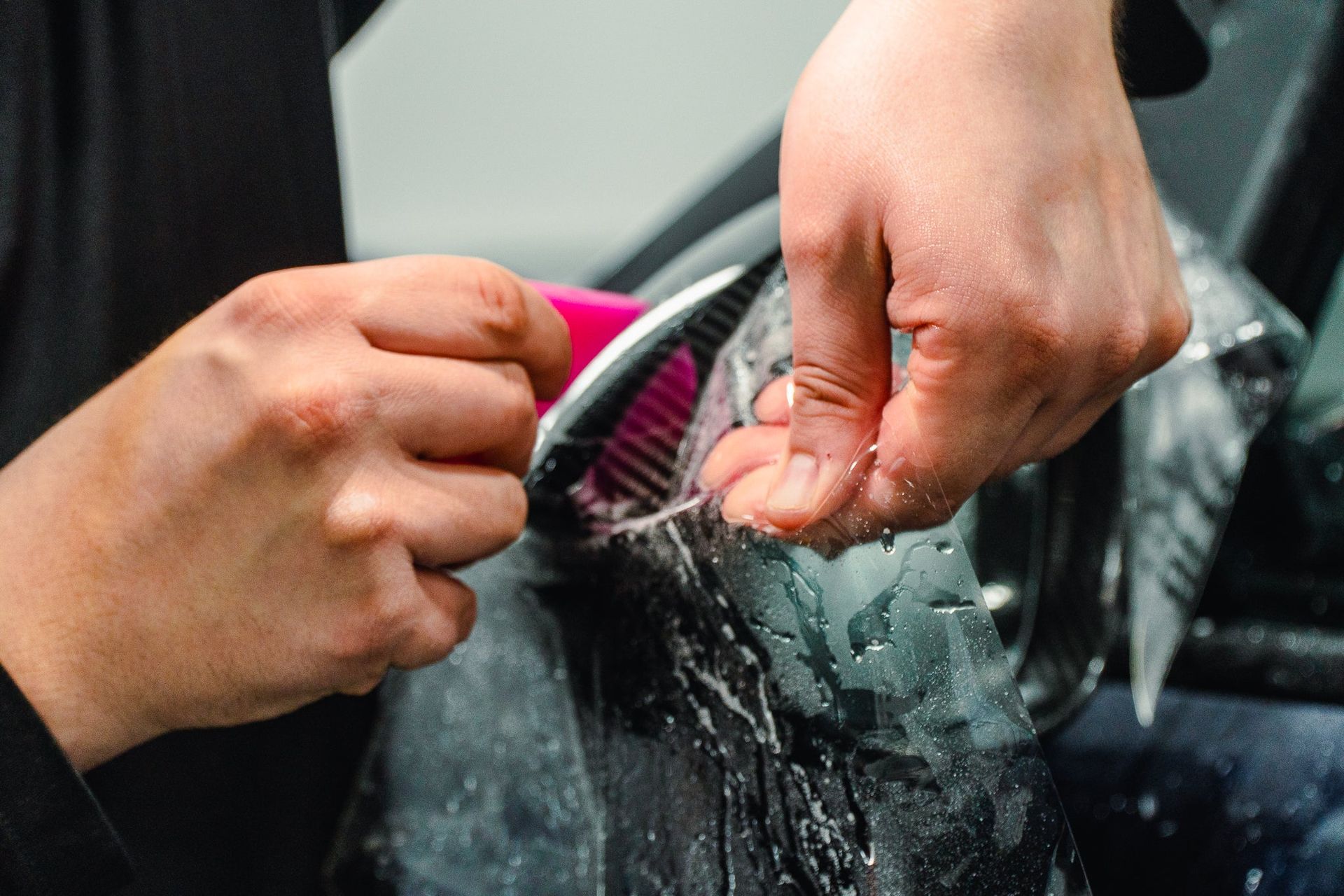 Hands cleaning a car window with a sponge and running water
