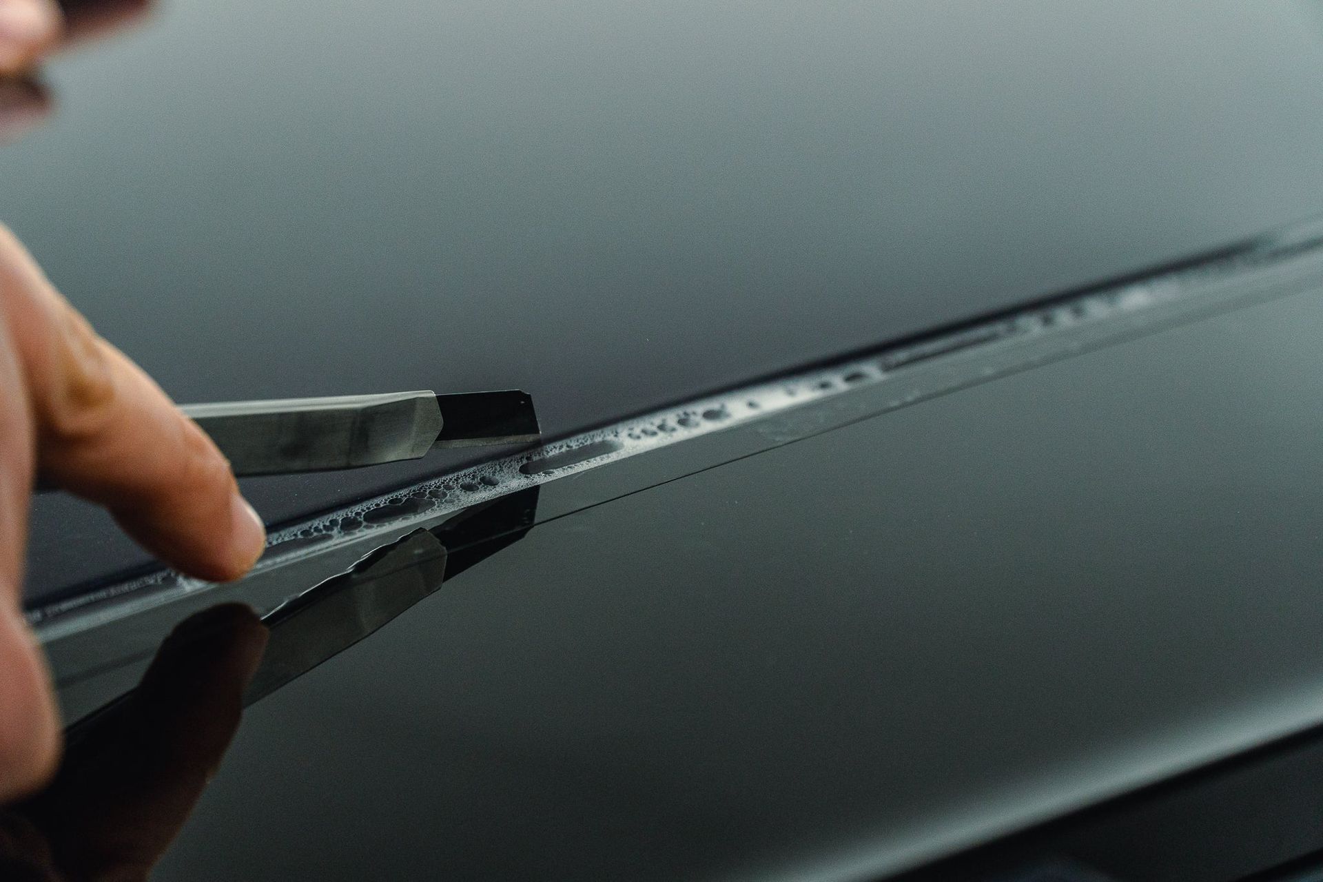 Hand wiping a dark car windshield with a squeegee, removing water droplets