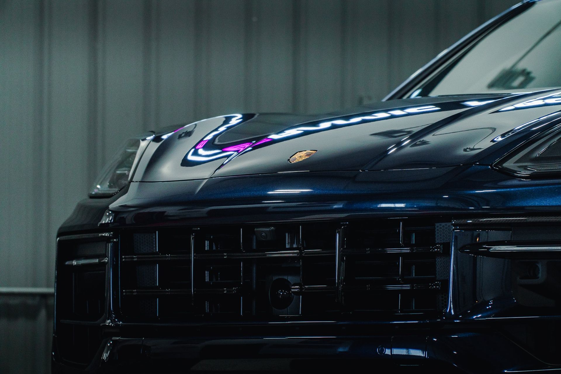 Front view of a dark blue sports car in a garage, with a glossy hood reflecting neon lights