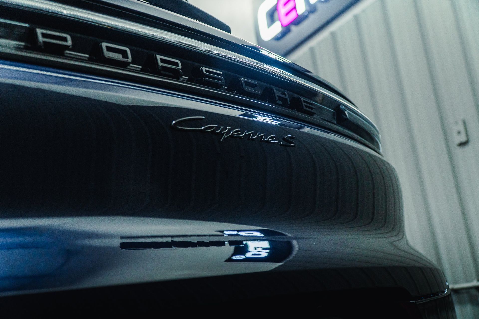 Close-up of a black car’s front grille and emblem in a garage or showroom, with chrome detailing