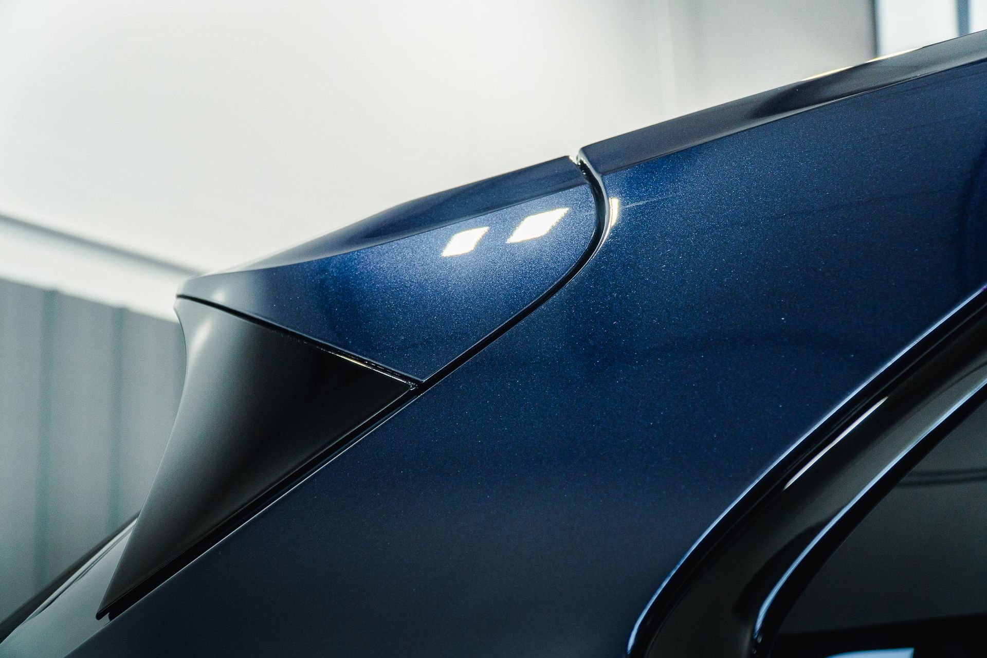 Close-up of a blue metallic car roof and rear pillar in a garage-like setting