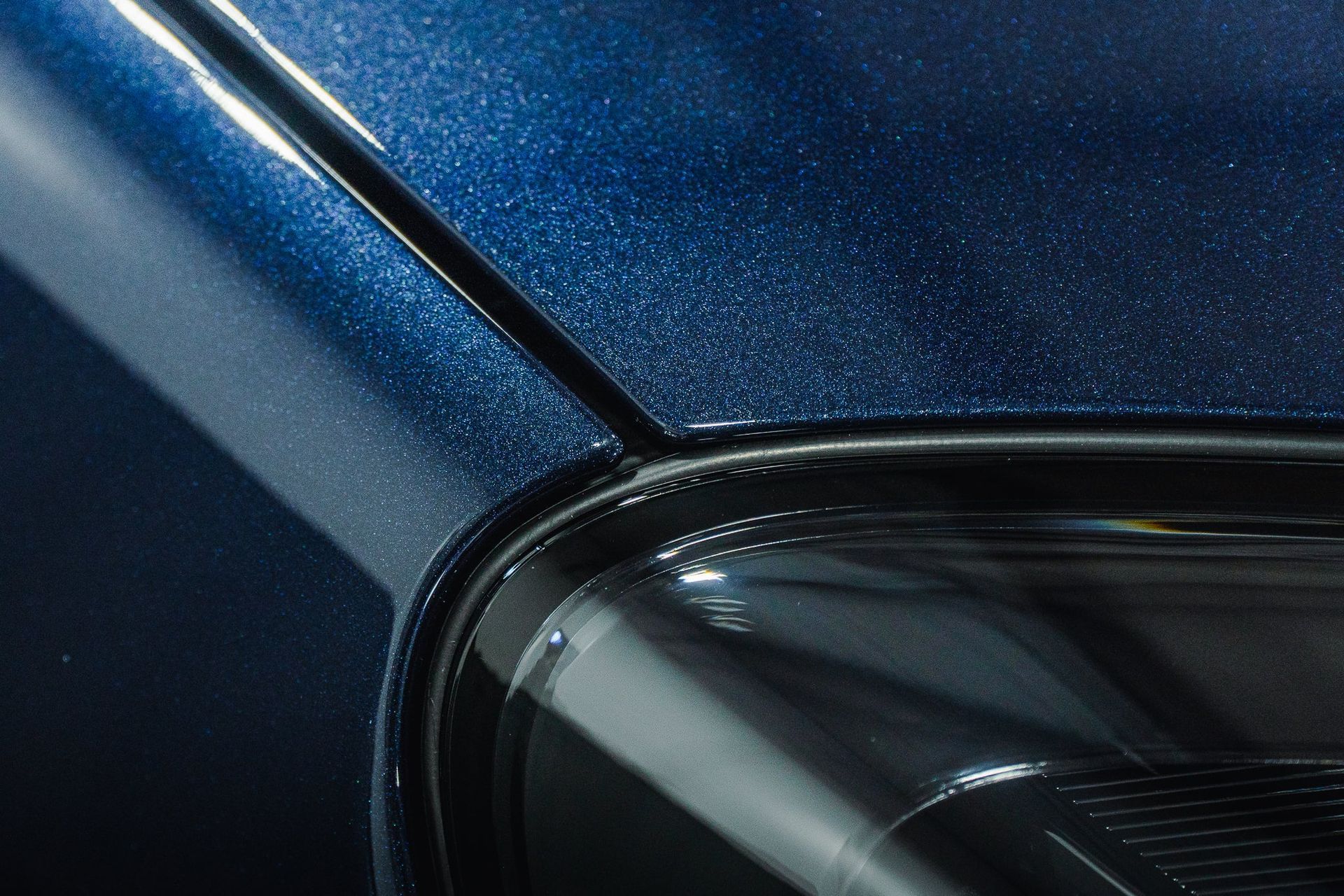 Close-up of a blue car’s front corner and headlight, showing glossy metallic paint and reflections