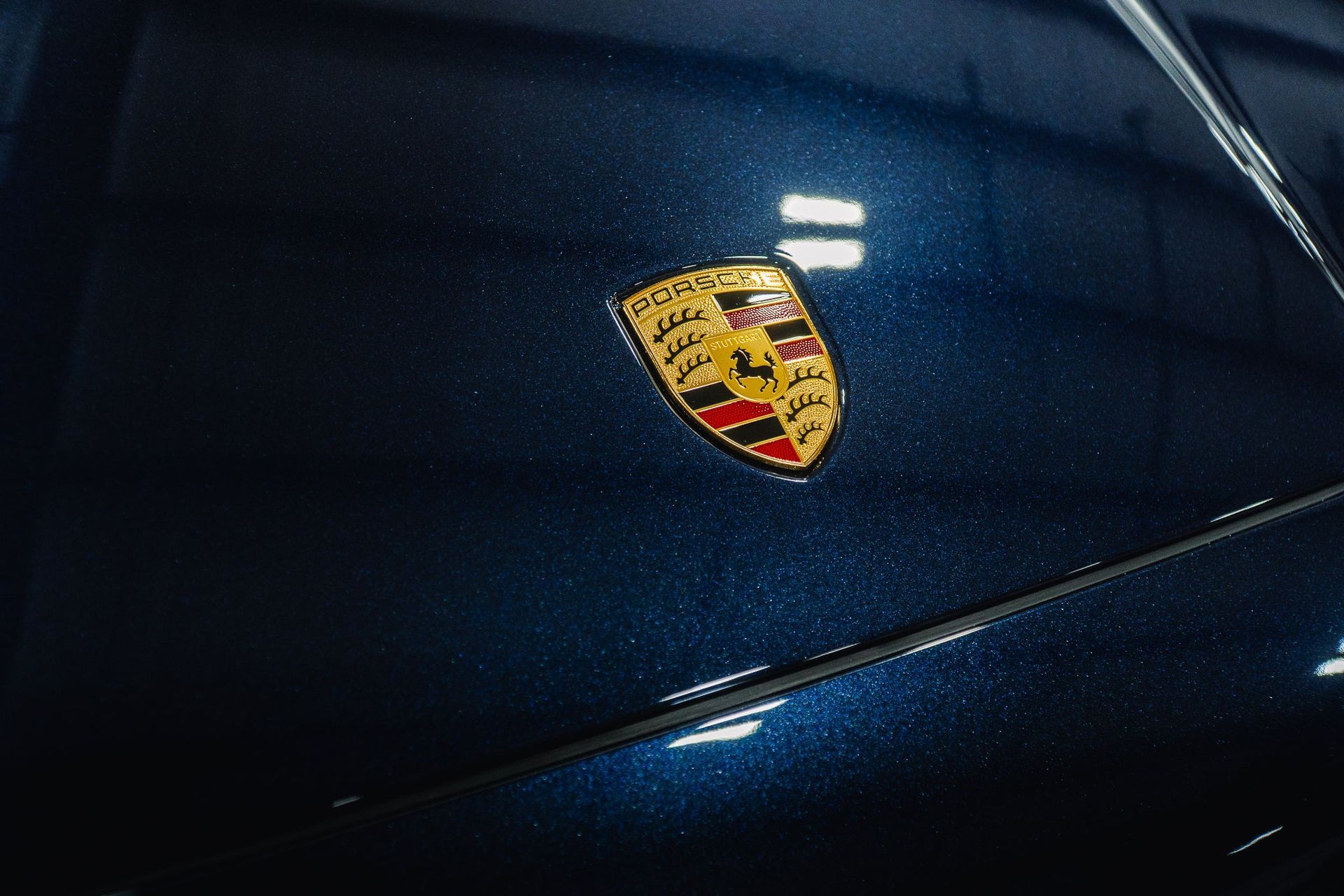 Close-up of a dark blue Porsche hood with the gold, red, and black crest emblem.