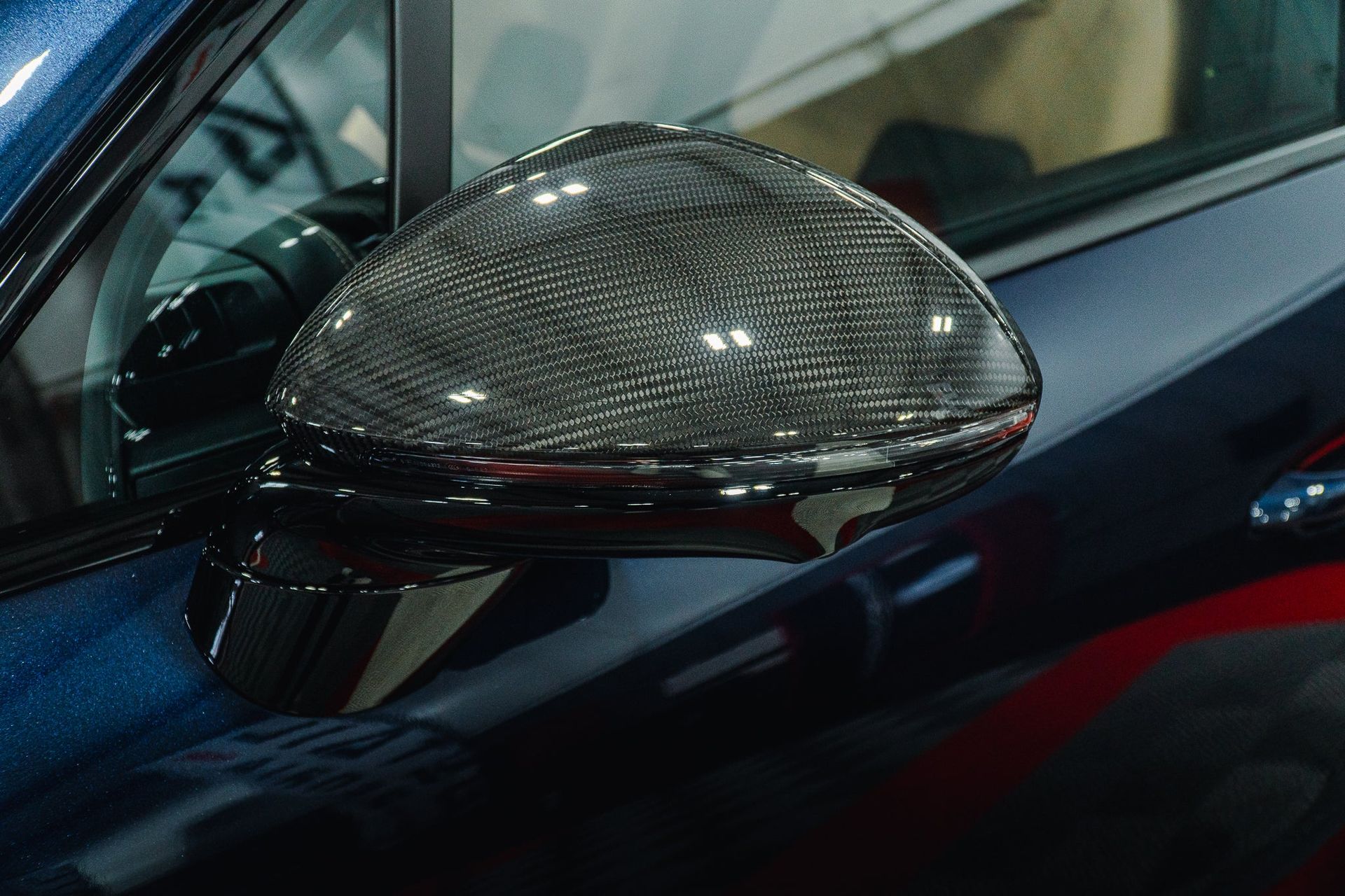 Carbon-fiber car side mirror on a dark blue vehicle, viewed close-up.