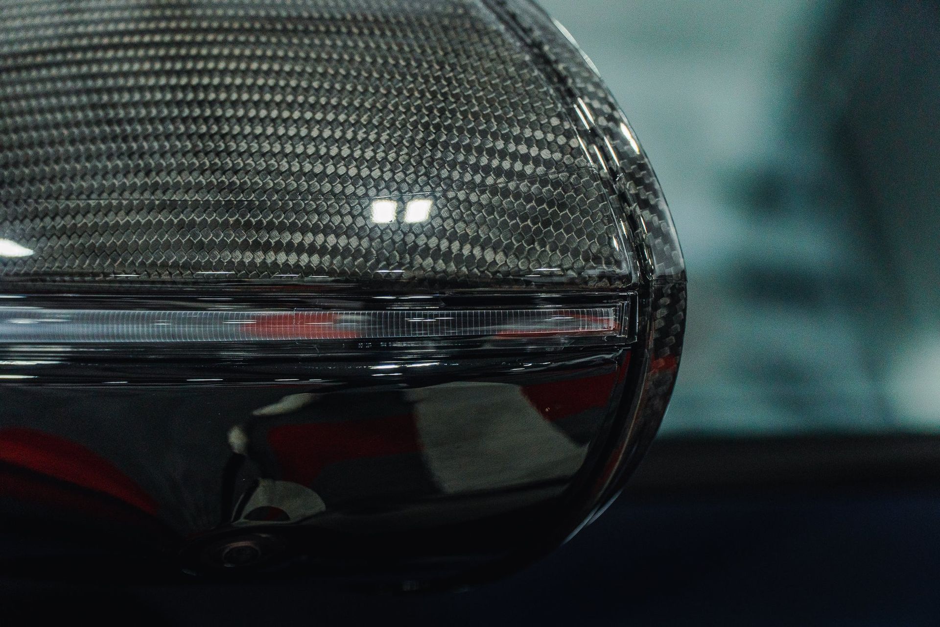 Close-up of a carbon-fiber car side mirror with a glossy black housing