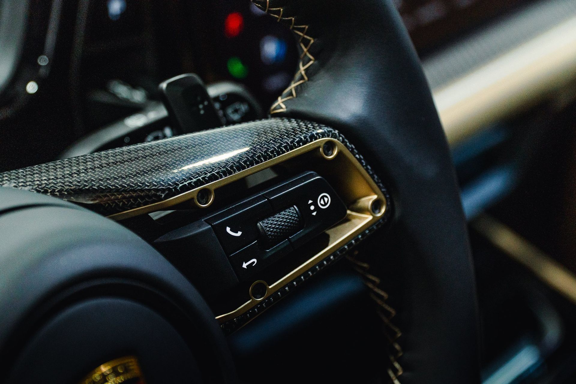 Close-up of a luxury car steering wheel with a digital control panel and carbon fiber trim