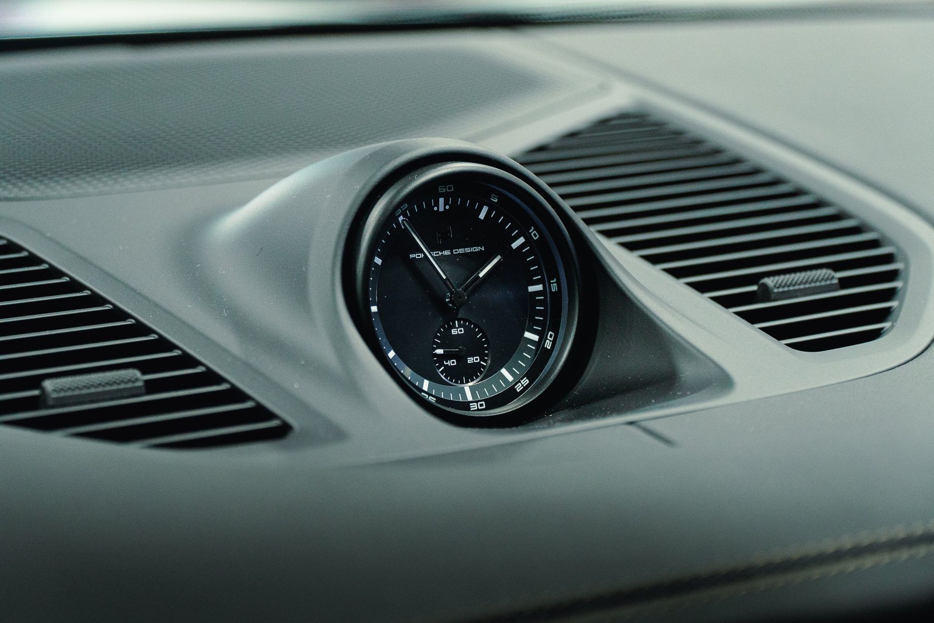 Black dashboard clock centered between car air vents on a gray console