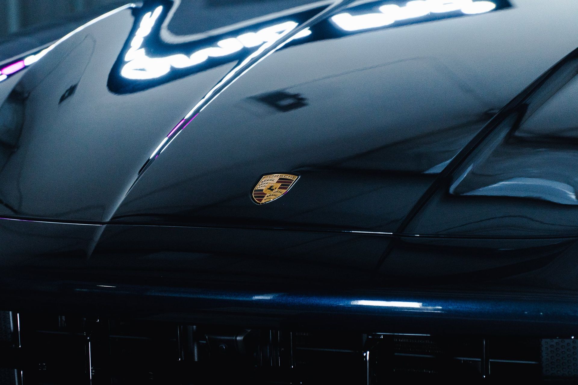 Close-up of a glossy dark blue Porsche hood with the gold crest emblem