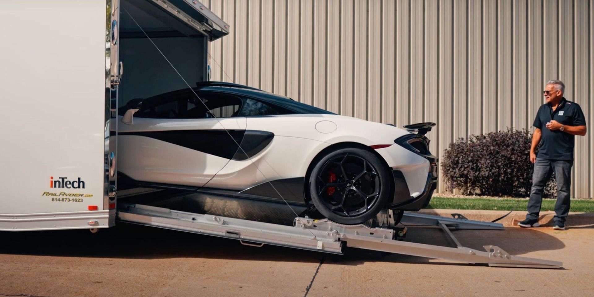 White sports car being loaded onto a trailer, with a man standing nearby outside.