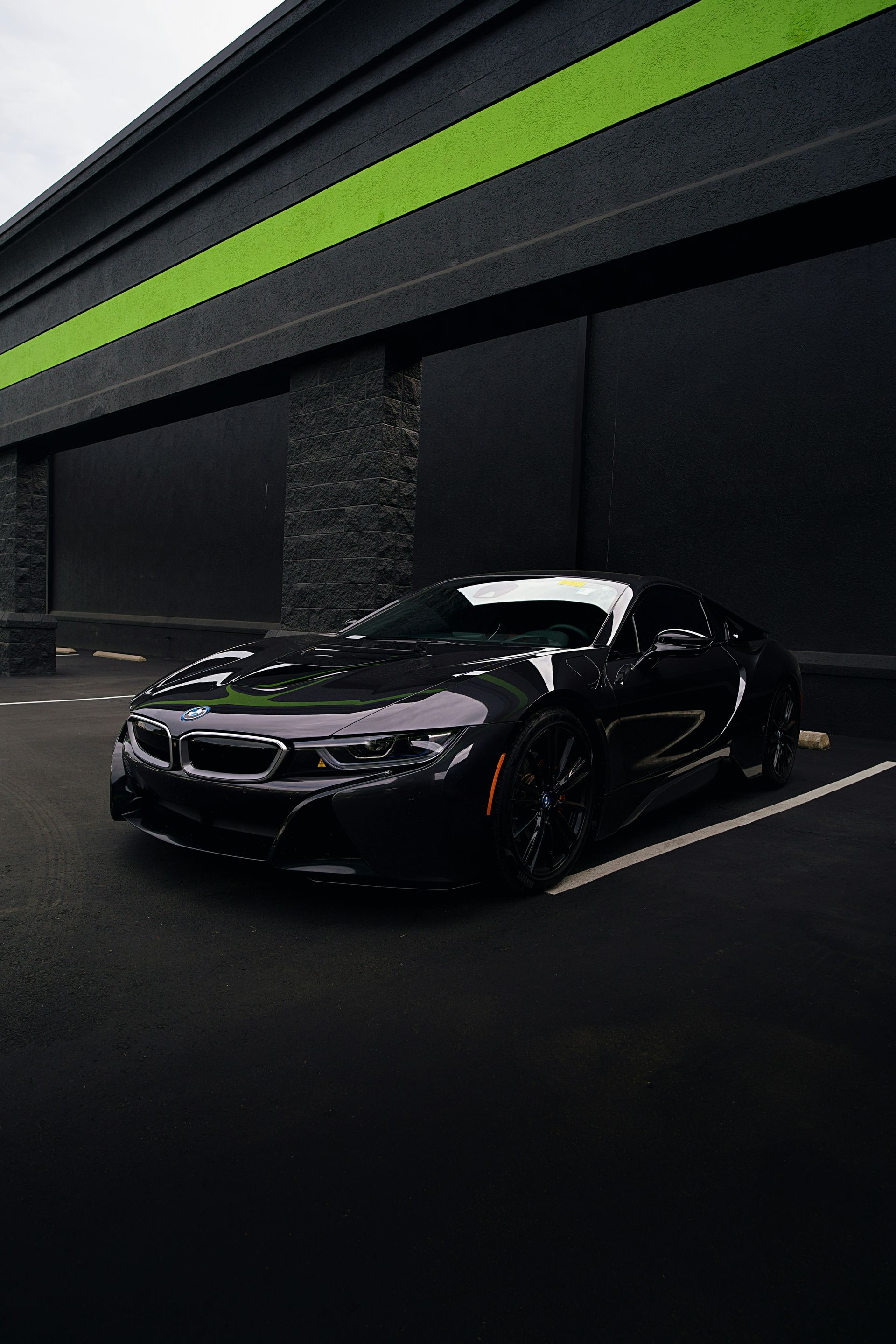 Black sports car parked in a dark lot beside a building with a bright green stripe