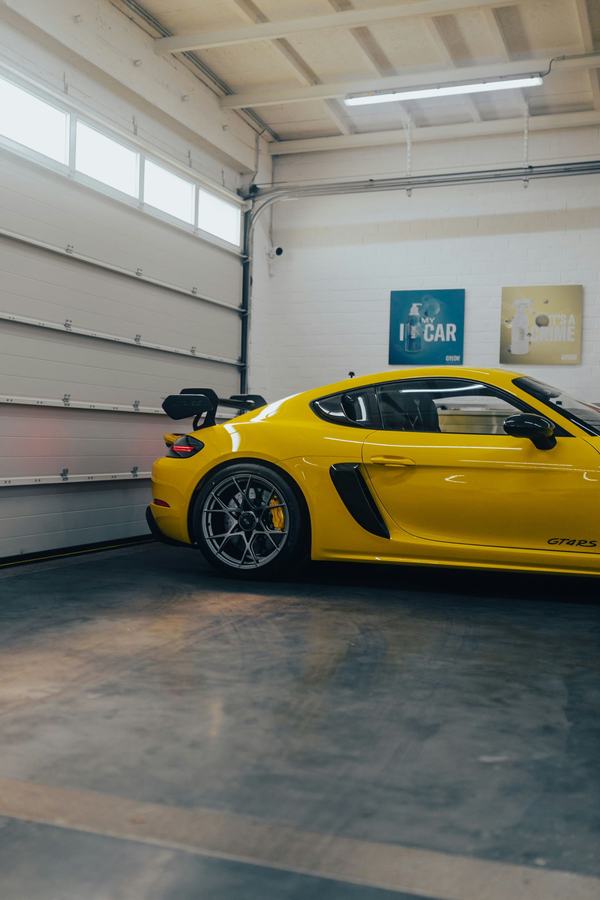 Yellow sports car parked inside a garage with a high rear spoiler and blue wall art.