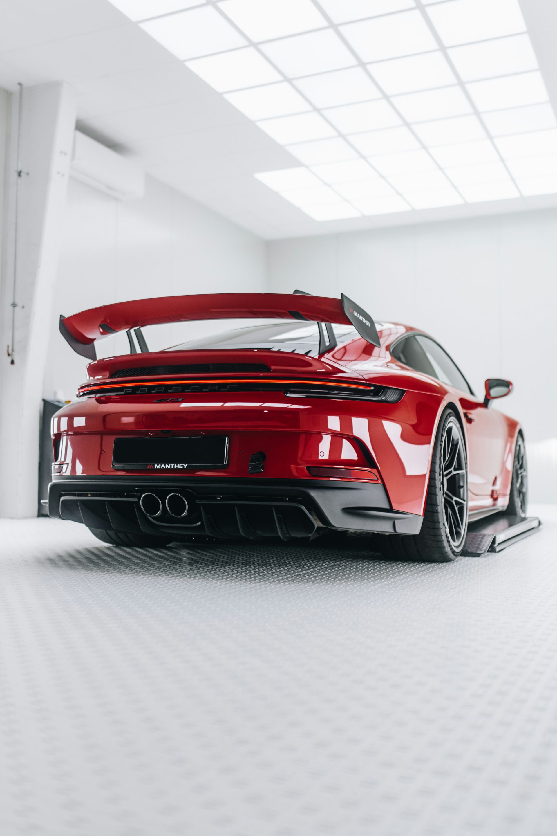 Red sports car in a bright white garage, viewed from the rear with a large spoiler.