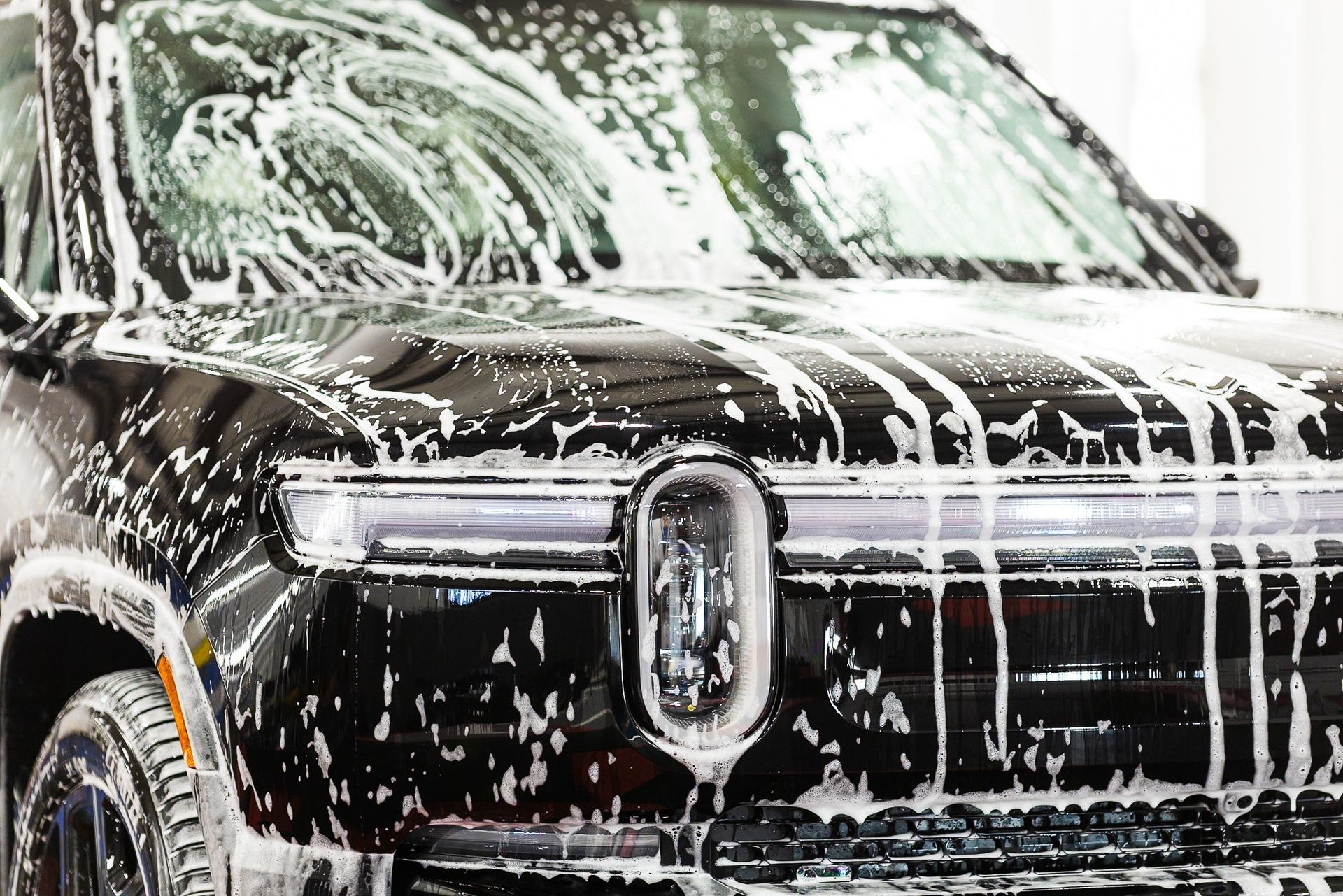 Black pickup truck covered in white soap suds during a car wash