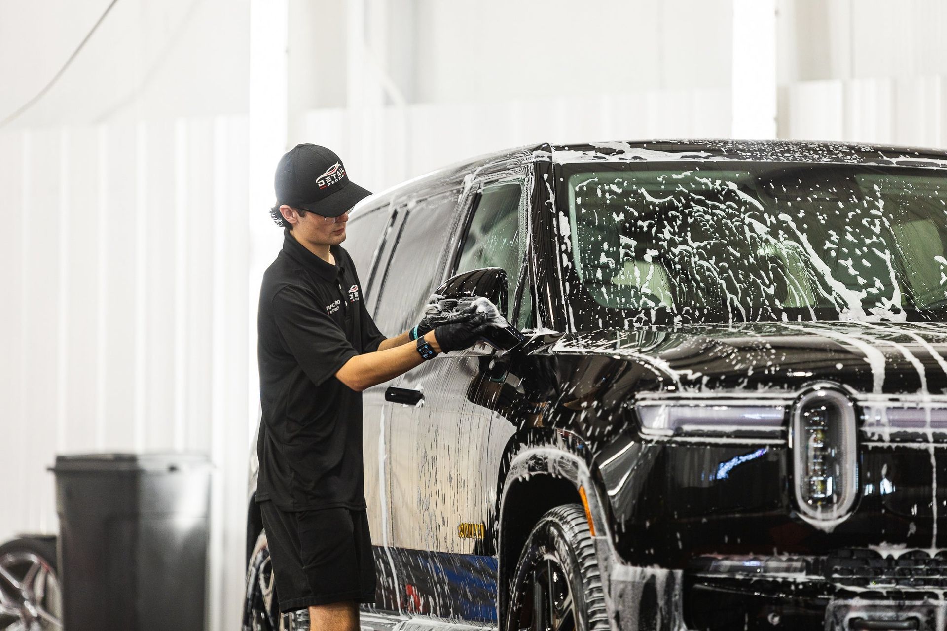 Person washing a black SUV in a soapy car wash bay