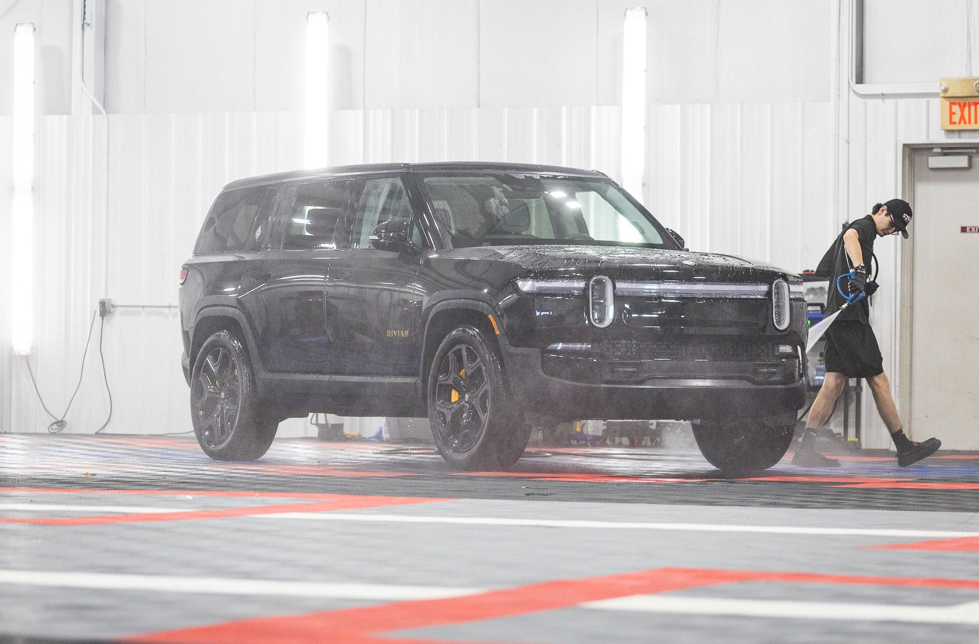 Black SUV in a bright garage with a person walking beside it, tires on a wet floor