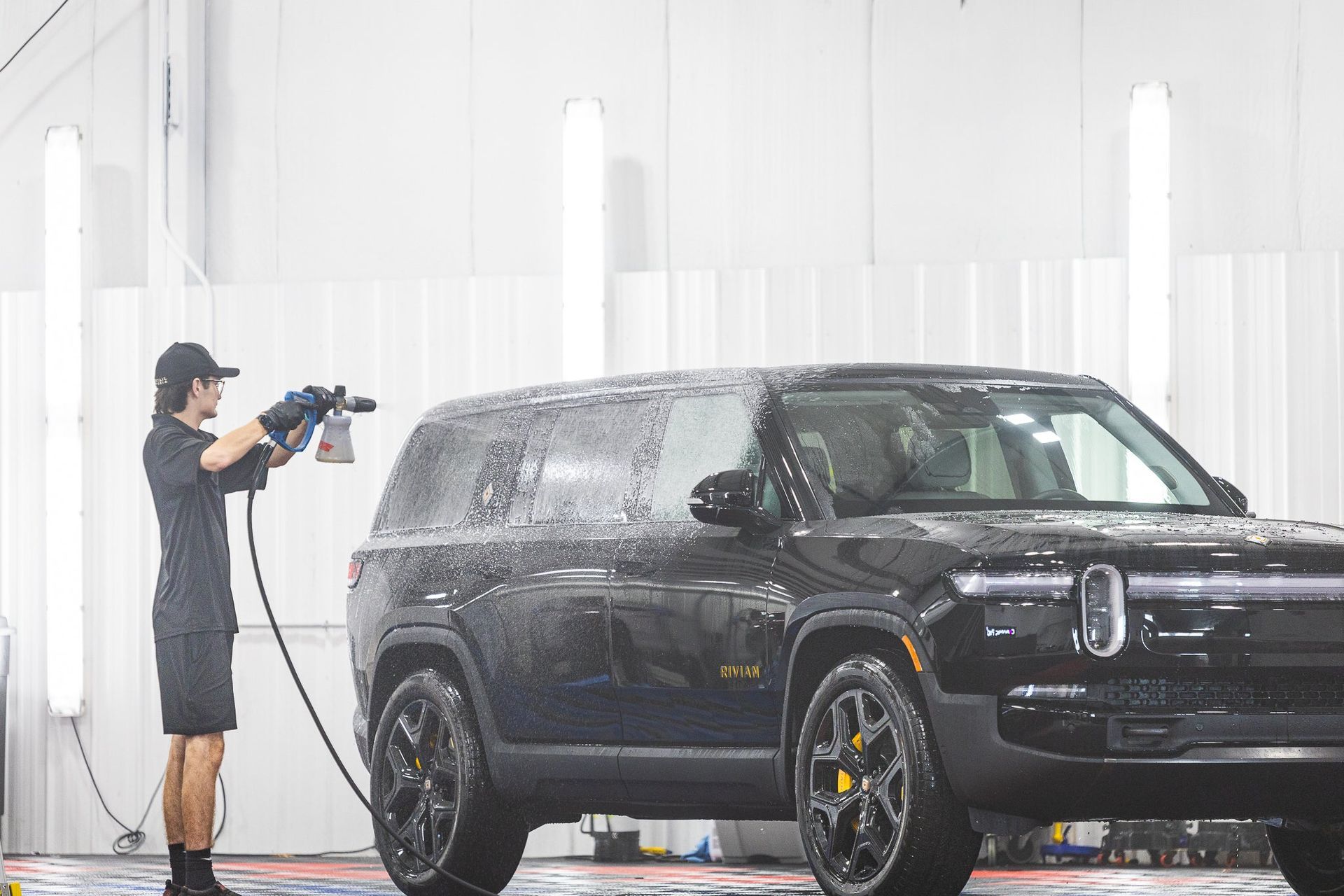 Person spraying a black SUV in a bright car wash bay