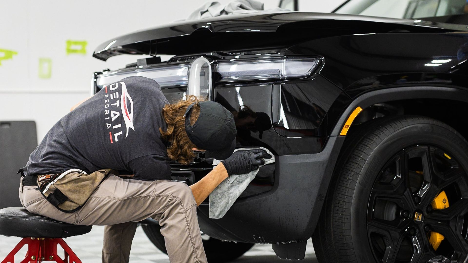 Mechanic working on the rear of a black car in a garage, with the wheel and taillight visible