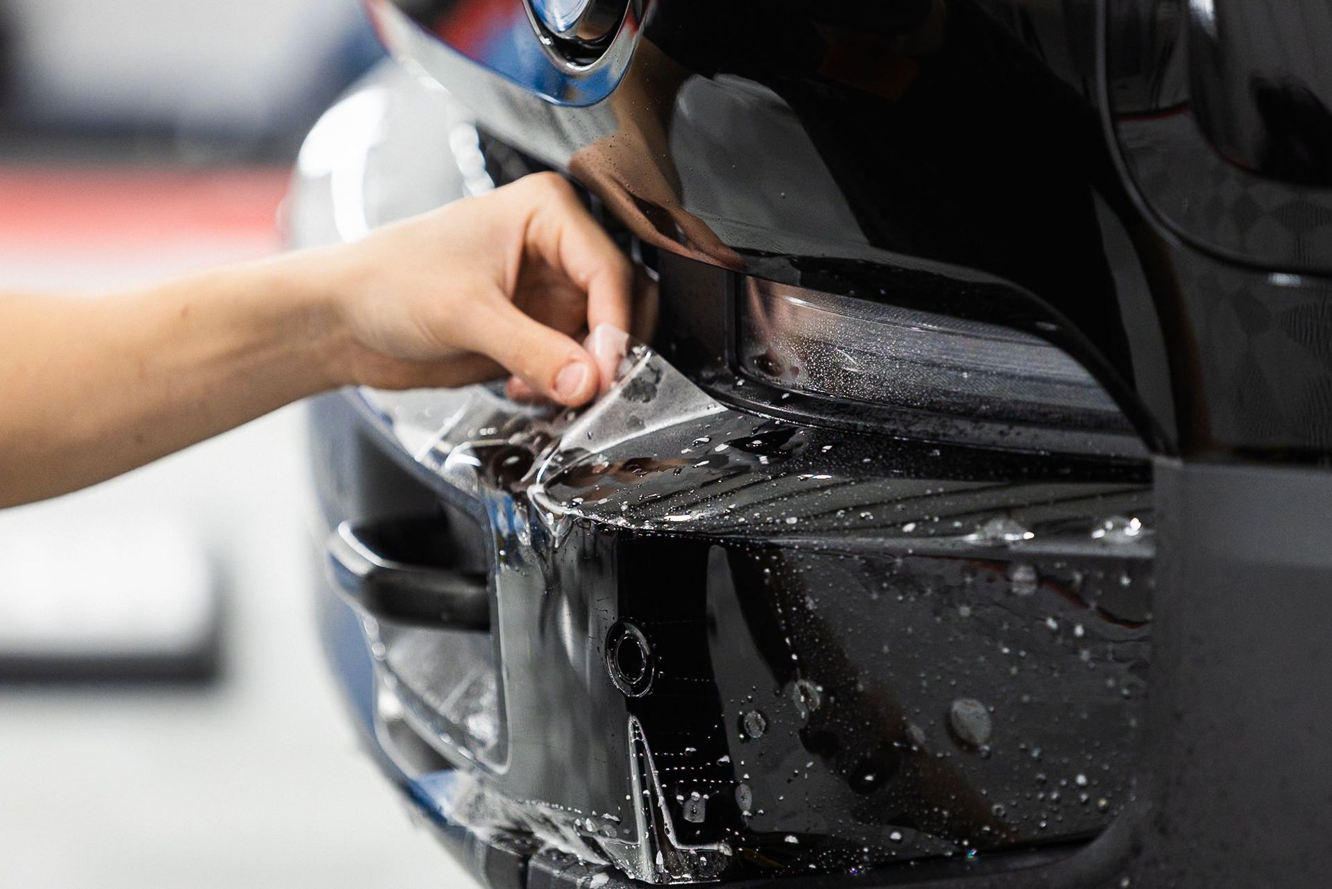 Hand washing a black car’s front bumper with water and soap foam