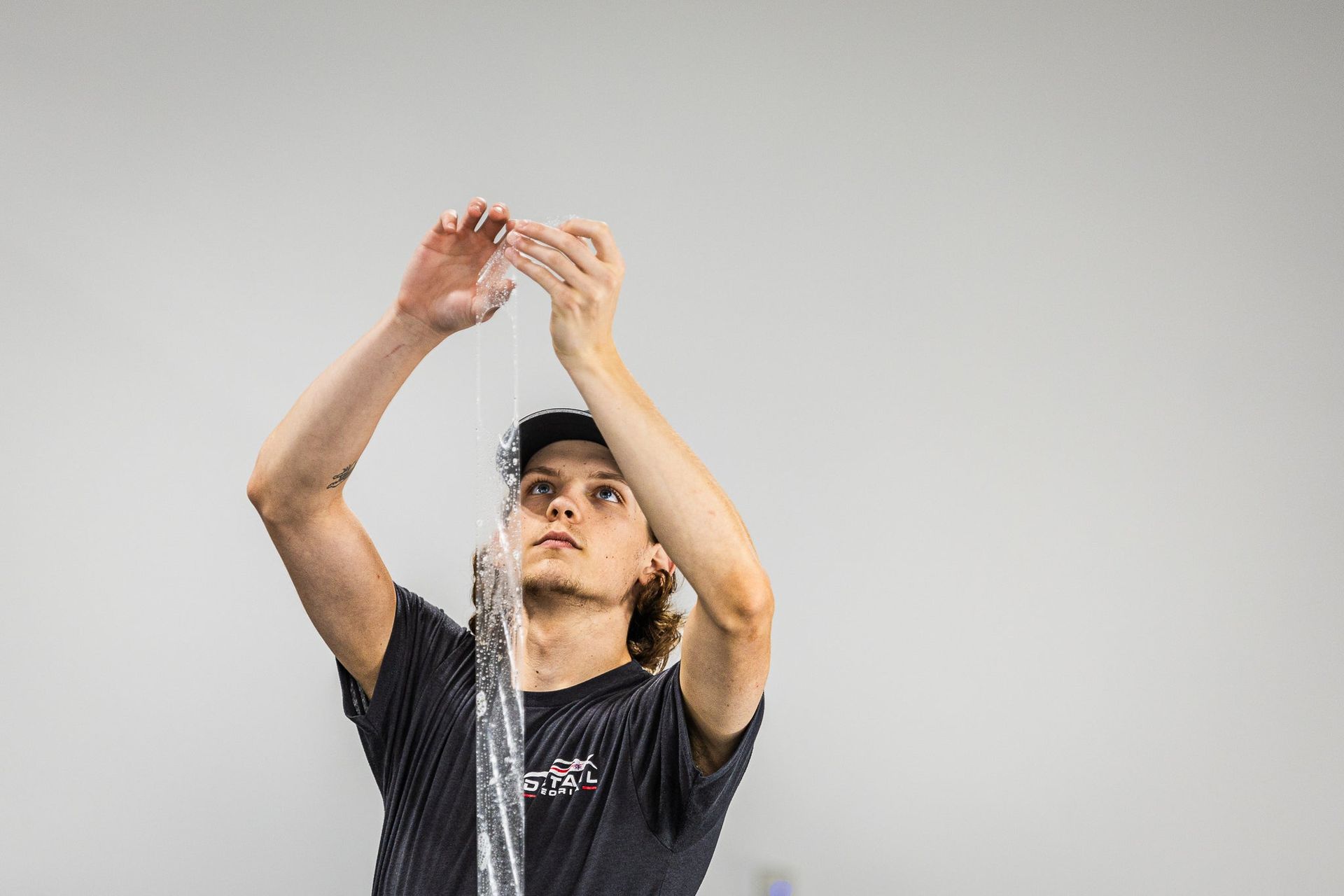 Person holding a string of water overhead against a plain background