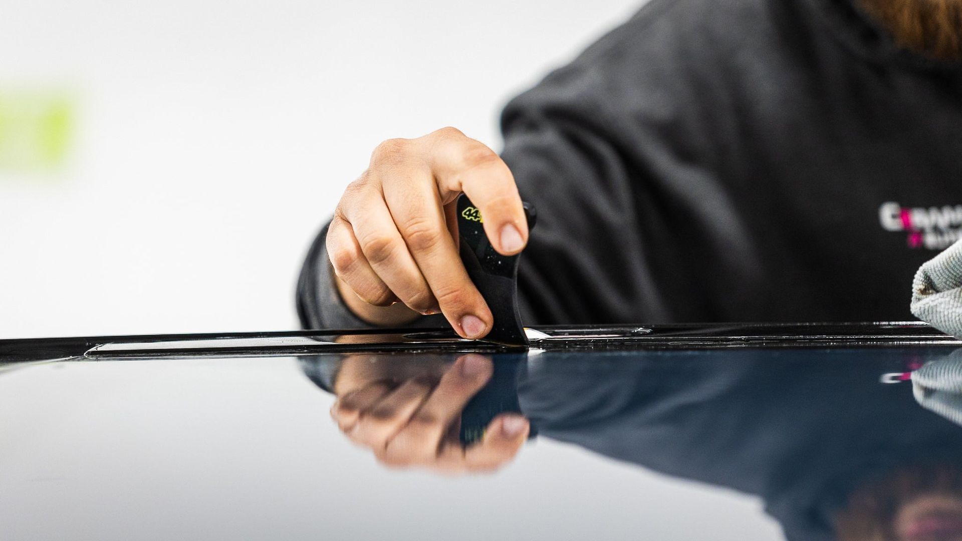 Hand resting on a glossy black car roof, with a blurred indoor background.
