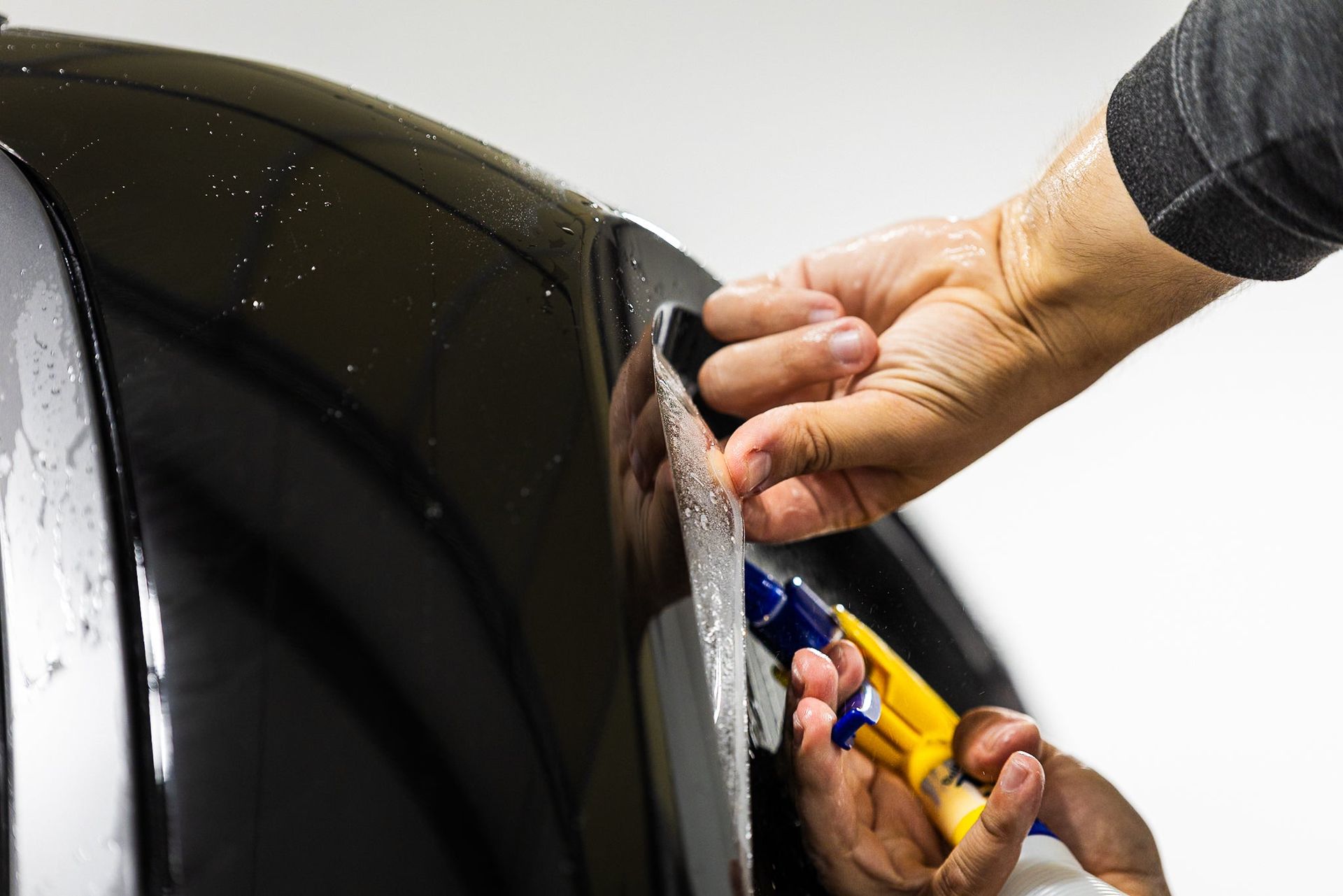 Hands using a plastic tool to pry open a black car panel.