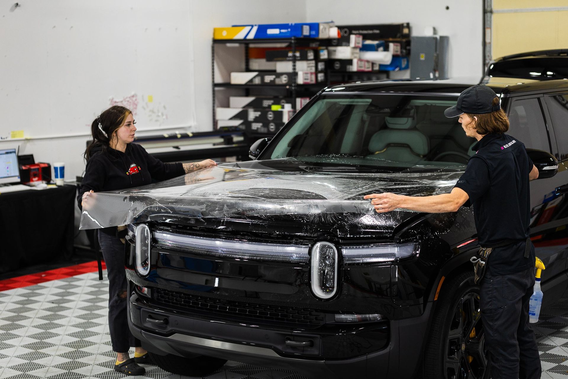 Two people washing a black SUV in a garage, covered in soap suds