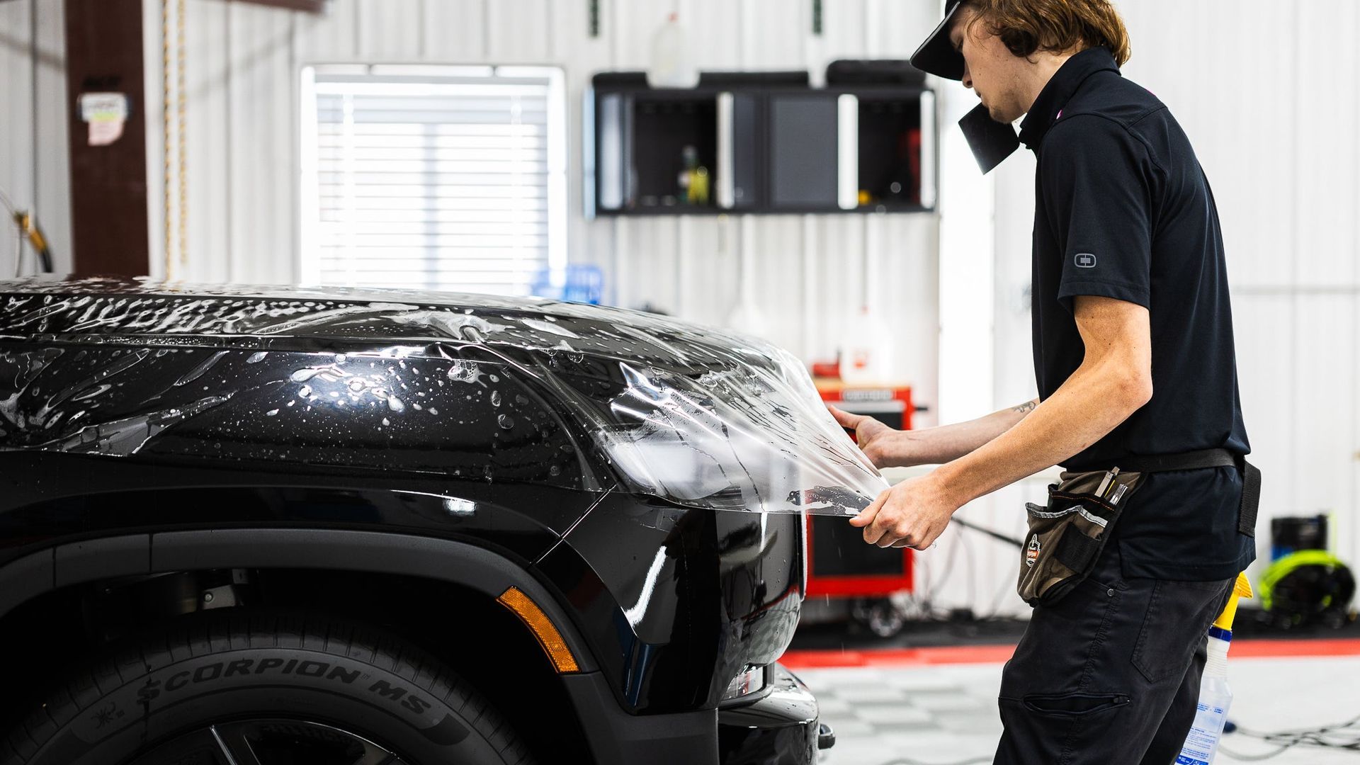 Mechanic polishing a black car in a bright auto shop